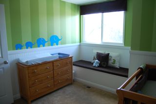 The aqua blue elephants march along the chair rail in the baby's changing area of the green and brown nursery.