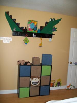 The large green alligator is painted on a solid beige color wall in a baby boy's nursery transforming a plain wall shelf into something spectacular!