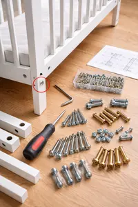 Crib screws missing with replacement hardware laid out beside a partially assembled crib frame
