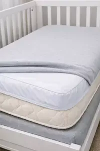 Crib mattress layered with a fitted sheet and a protective waterproof mattress cover underneath