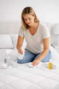 Woman cleaning a mattress with simple household supplies in a bright bedroom