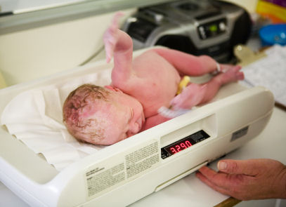 A newborn infant being weighed with a digital baby scale on a custom nursery changing table