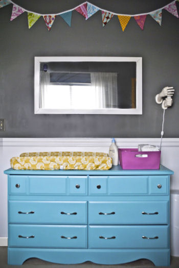 This baby girl's nursery has charcoal gray walls accented with bright colors including a turquoise blue dresser.