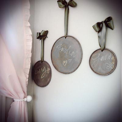 A wall display of Restoration Hardware chalkboards hung with wide, chocolate brown satin ribbons tied in bows in a baby girl nursery