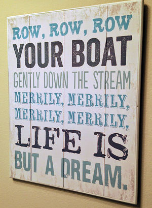 A  rustic sign with a line from the popular row row row your boat nursery rhyme used as wall décor in a baby boy nautical nursery