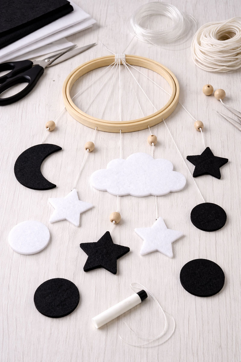 DIY black and white crib mobile layout showing felt shapes hanging from a wooden hoop before final adjustment