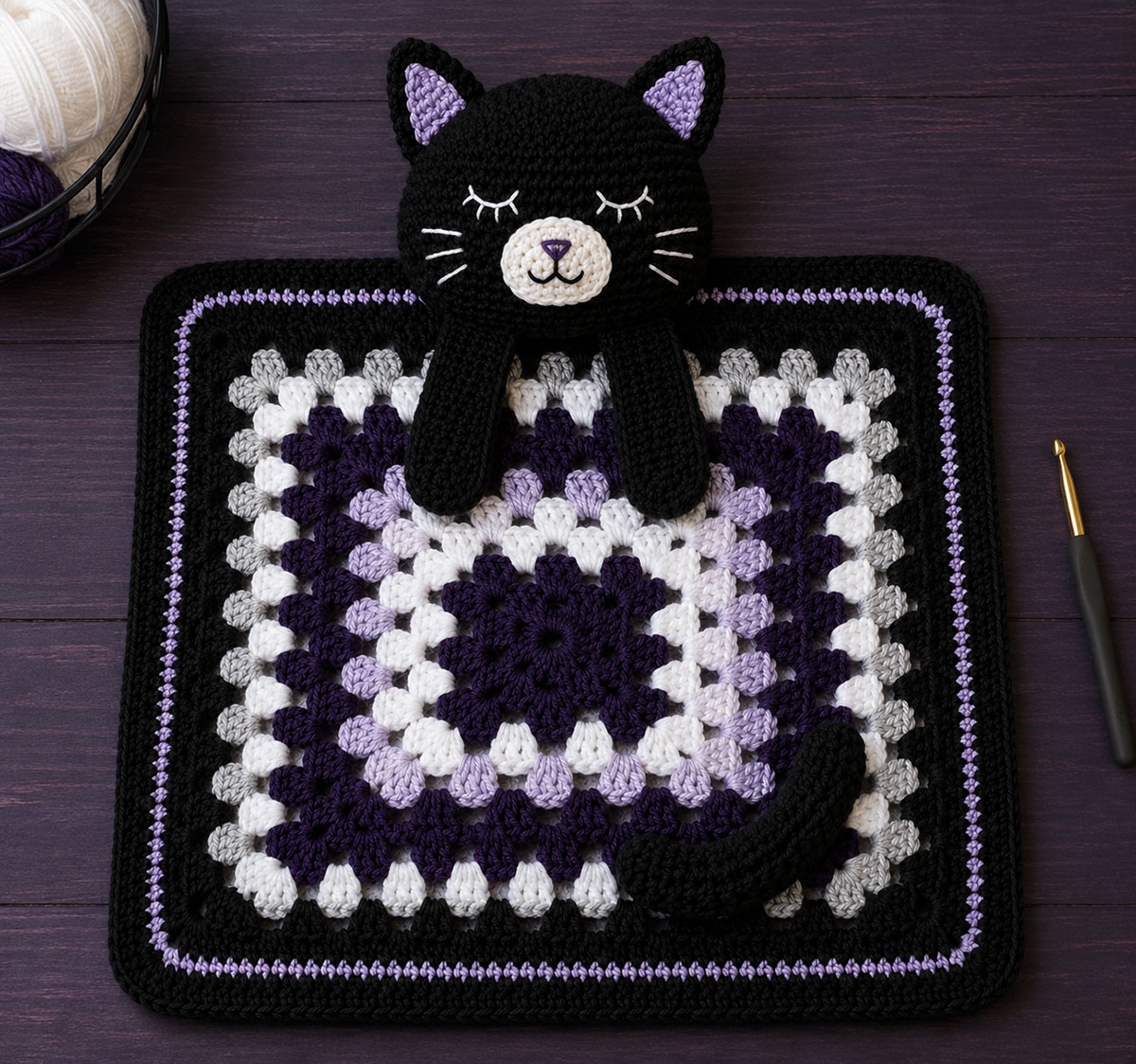 Black cat crochet head paws and curved tail arranged on the blocked granny-style blanket before sewing