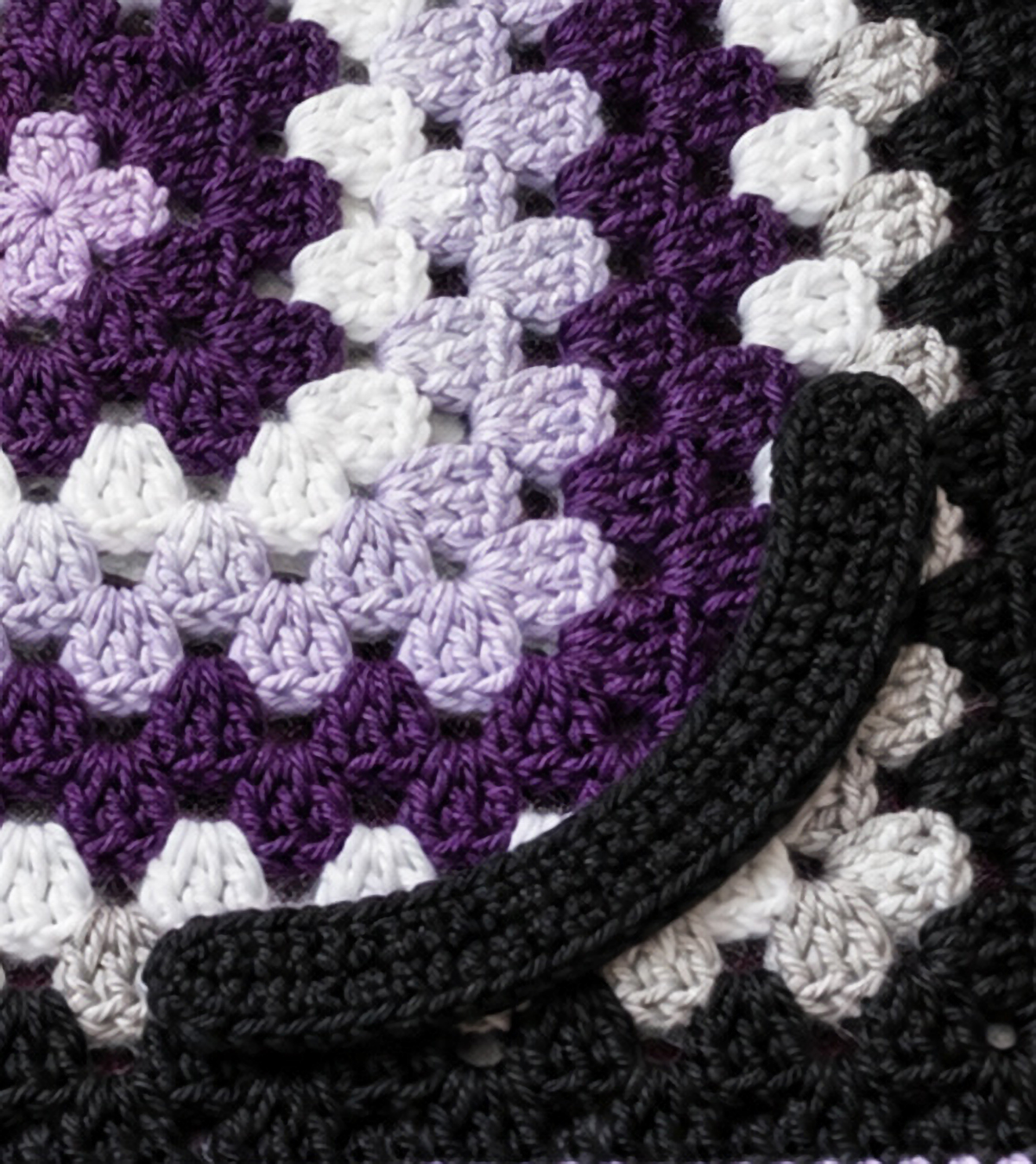Finished unstuffed black crochet cat tail arranged in a gentle curve beside the lovey blanket in a close side-angle photograph