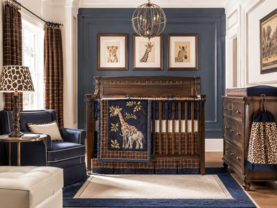 Blue and brown baby boy nursery with dark wood crib, handmade safari animal bedding, leopard-print curtains, giraffe lampshade and navy upholstered chair.
