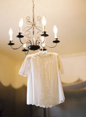 Vintage baby dress on a hanger displayed on an antique chandelier in a nursery setting
