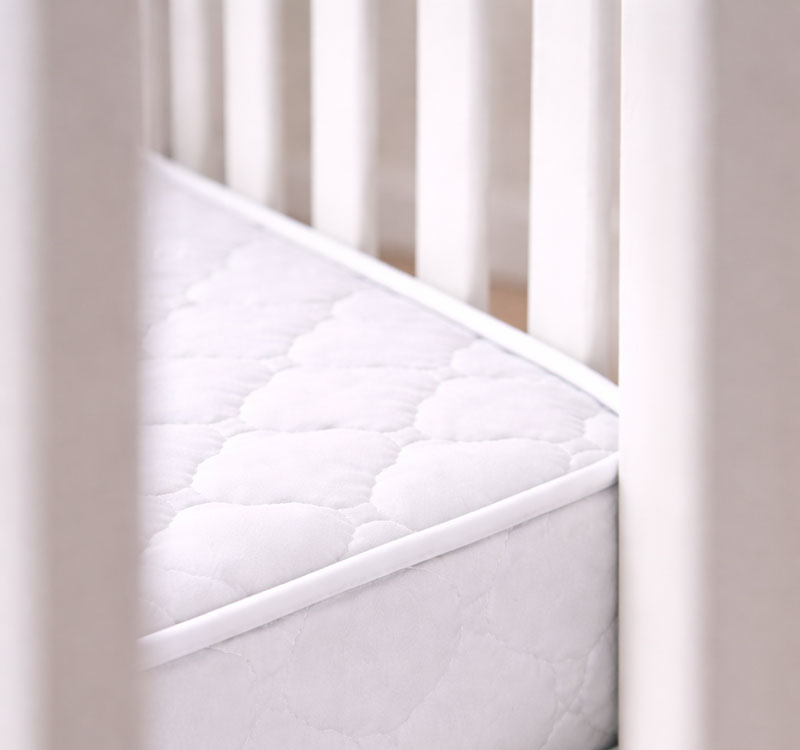 Close-up of a crib mattress edge showing a small space between the mattress and the crib rail