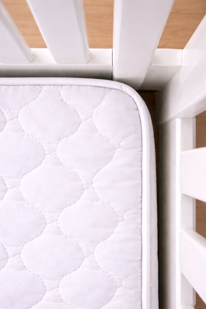 Corner view inside a standard white crib showing one mattress and a slightly uneven gap near a corner