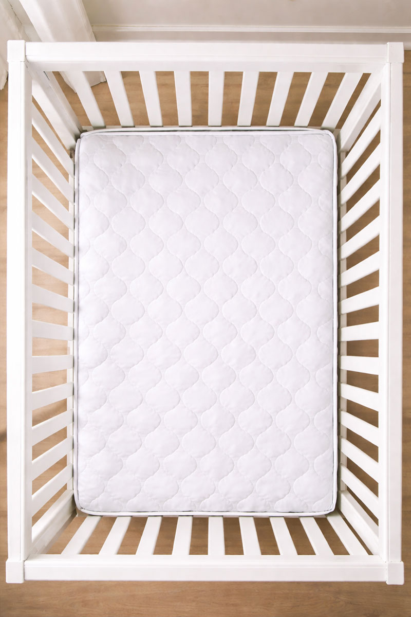 Top-down view of a standard white crib with one crib mattress showing a small gap along the rails