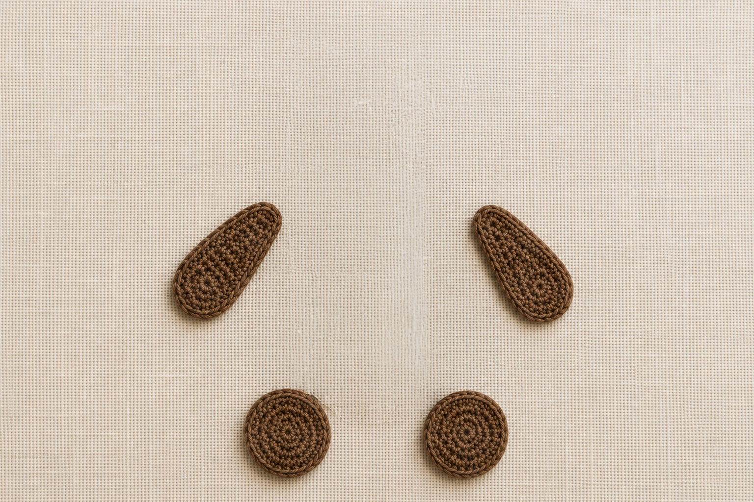 Matching flat brown crochet bear arms and two separate rounded crochet feet arranged beside a crochet hook