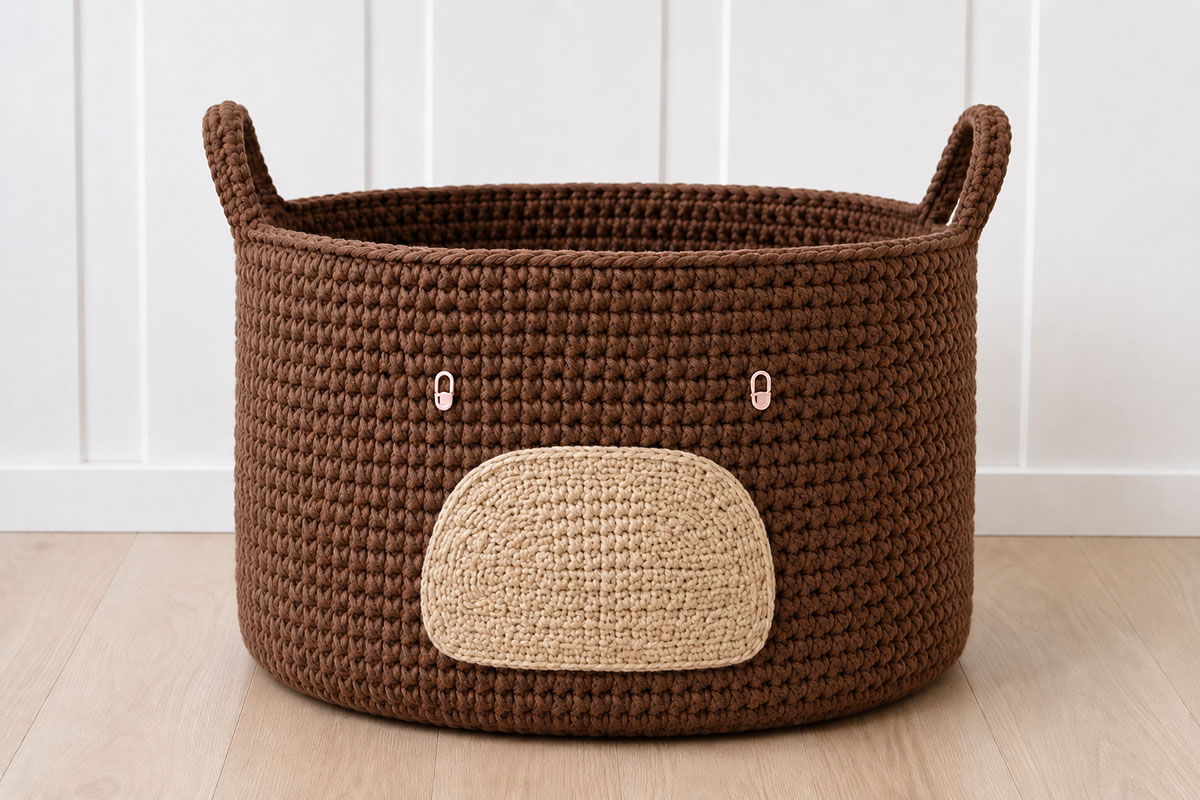 Front of a brown crochet bear basket with tan muzzle and removable markers showing evenly spaced eye positions before embroidery
