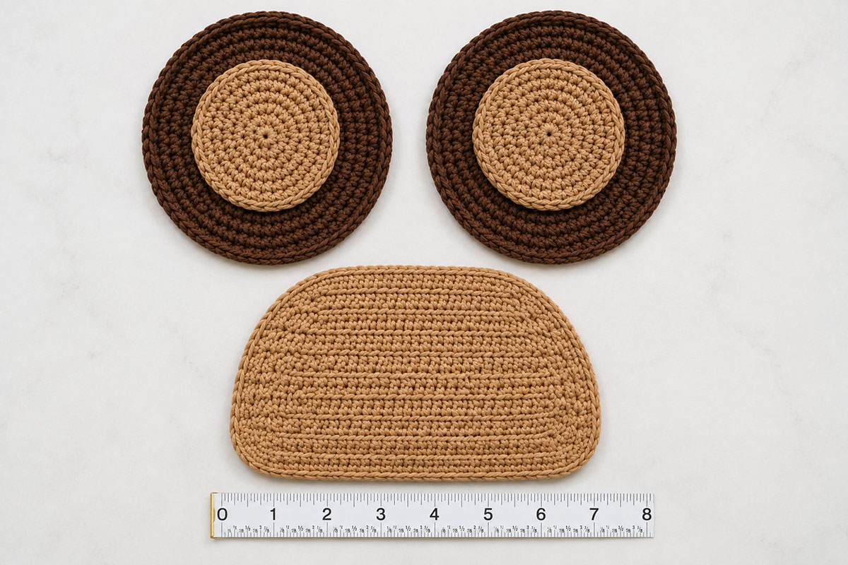 Tan crochet bear muzzle measuring about seven inches wide beside two completed layered bear ears before assembly