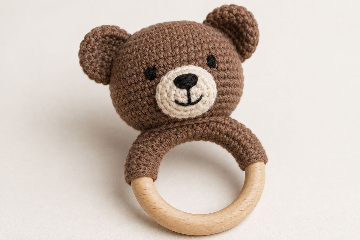 Brown crochet bear head with warm ivory embroidered face securely sewn across the crocheted upper section of a natural wooden rattle ring while the lower part of the wood remains exposed