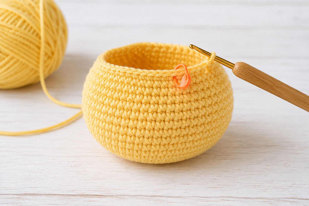Yellow crochet duck body in progress with a rounded lower section and stitch marker showing the continuous rounds