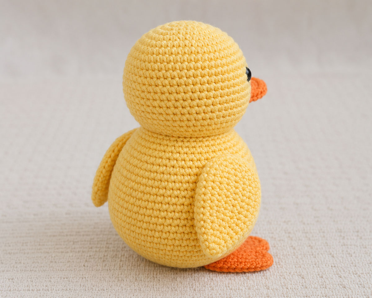 Back and side view of the finished yellow crochet duck showing the smooth neck seam and two matching flat wings