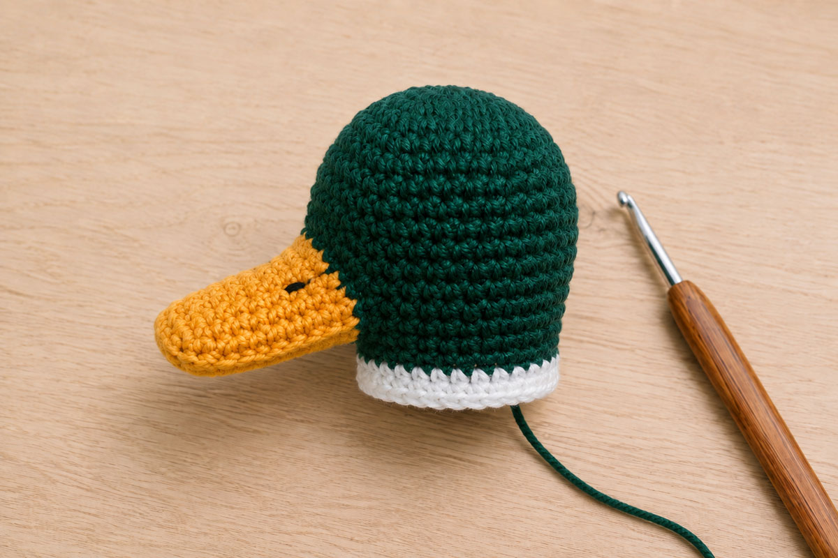 Side view of a crochet mallard green head with a flat golden yellow bill and small embroidered black nostrils