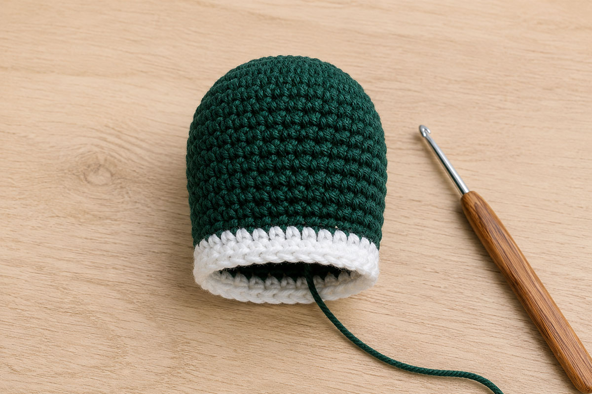 Crochet mallard head in deep green yarn with a narrow white neck ring and an open base ready for assembly