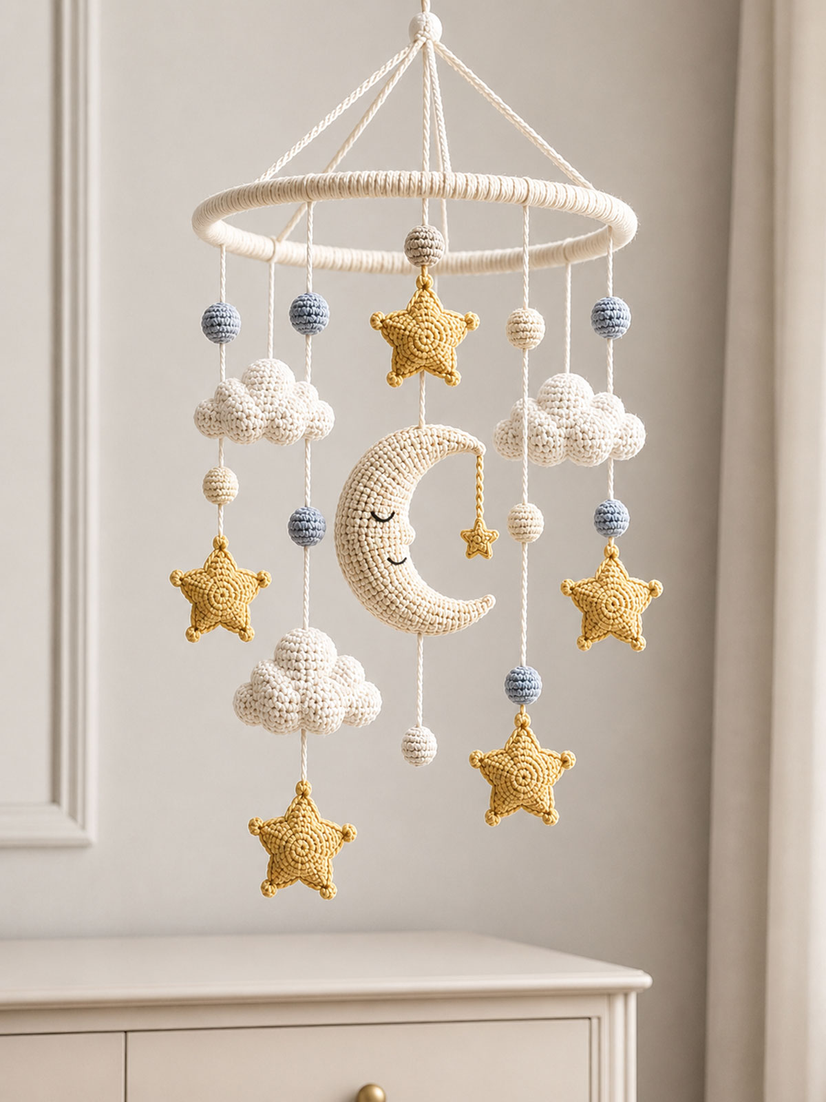 Crochet moon and five point stars hanging from a wooden nursery mobile above a dresser