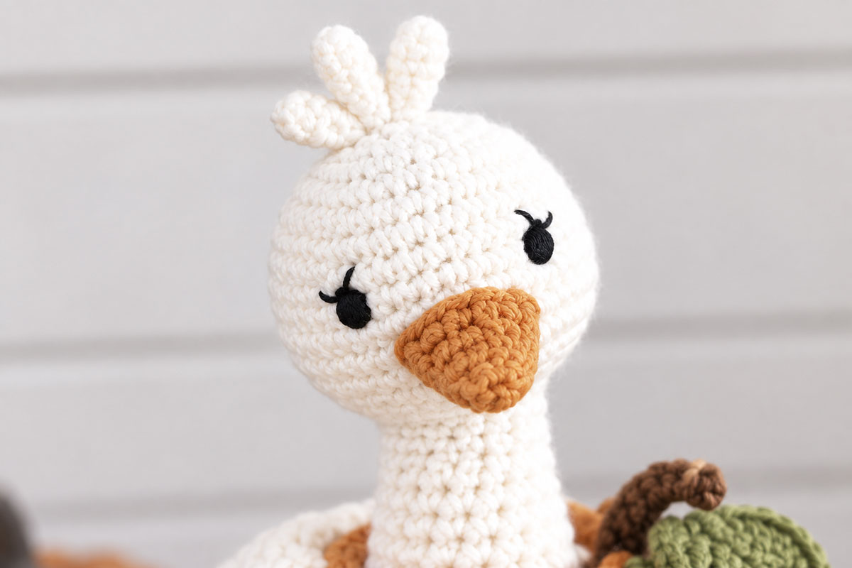 Close view of crochet pumpkin goose with black satin stitch eyes embroidered eyelashes orange bill and three white crown feathers