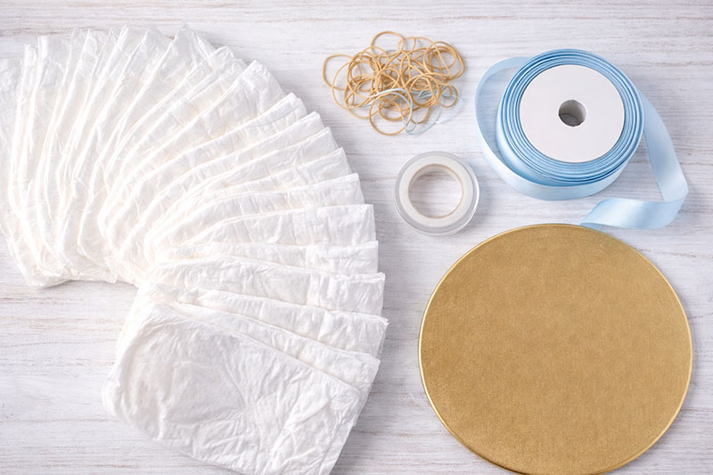 Supplies for making a diaper cake including diapers, ribbon, rubber bands, and cake base