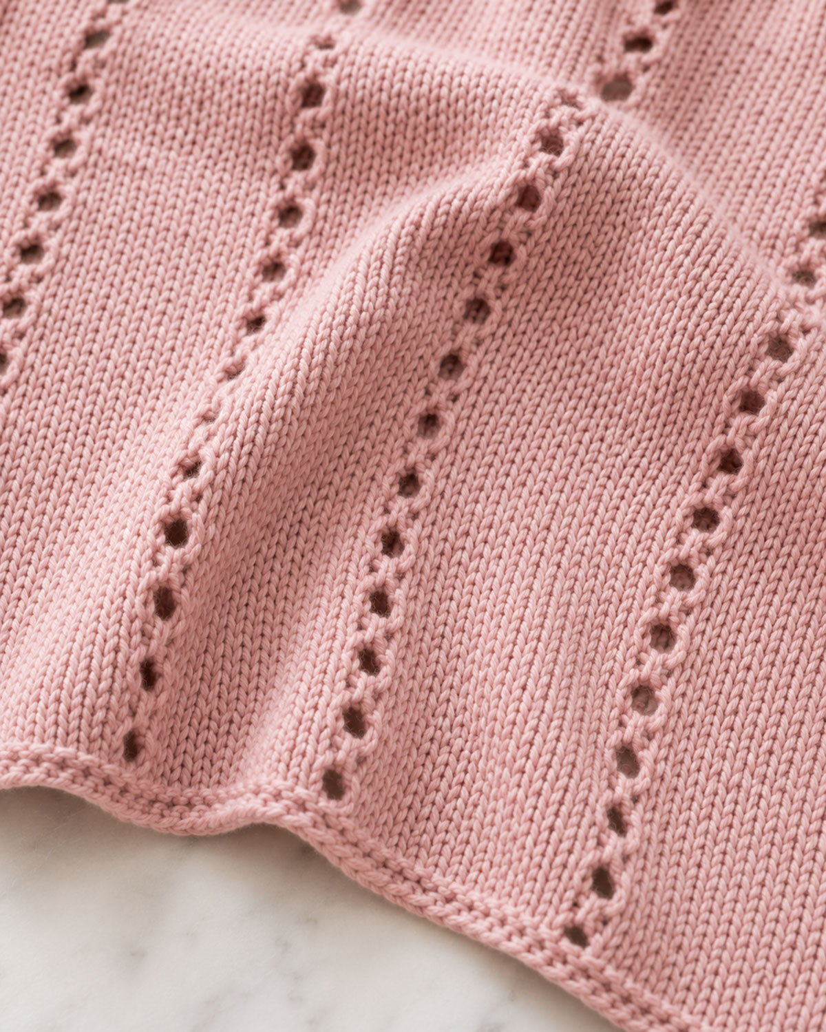Close view of the knitted baby blanket eyelet repeat with yarn-over openings and three-stitch side edge