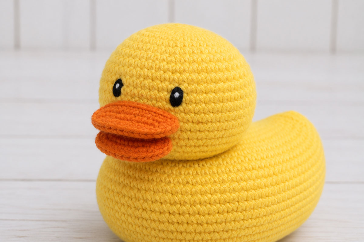 Crochet rubber duck face with black satin-stitch eyes and one tiny white highlight stitch in each eye