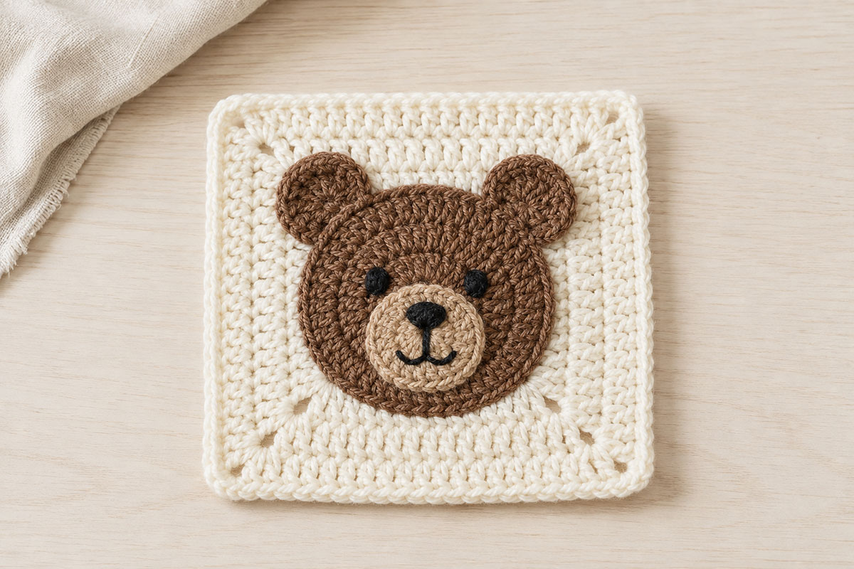 Finished teddy bear granny square with a brown crochet head rounded ears tan muzzle and embroidered eyes nose and mouth