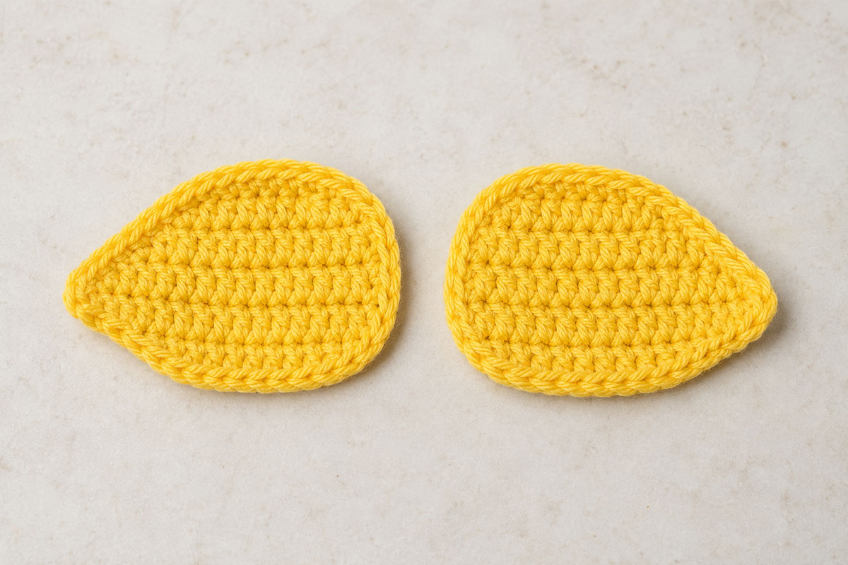Two matching unstuffed yellow crochet duck wings lying flat side by side before assembly