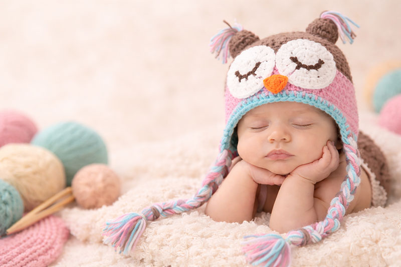 Sleeping baby wearing a handmade crochet owl hat on a soft neutral blanket