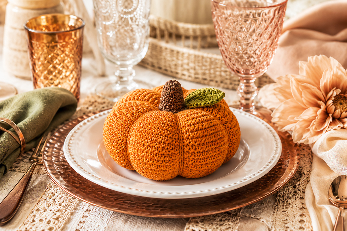 Free crochet pumpkin pattern showing a stuffed orange ribbed pumpkin with brown crocheted stem and green leaf