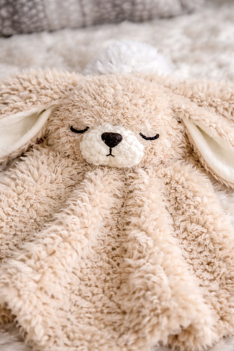 Close-up of a fuzzy crochet bunny lovey with floppy ears and a soft crocheted nose
