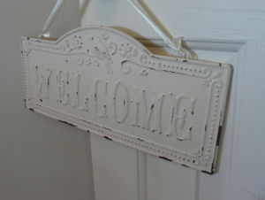 A chipped white painted vintage welcome sign on the door to a baby girl shabby chic nursery in pink gray and white