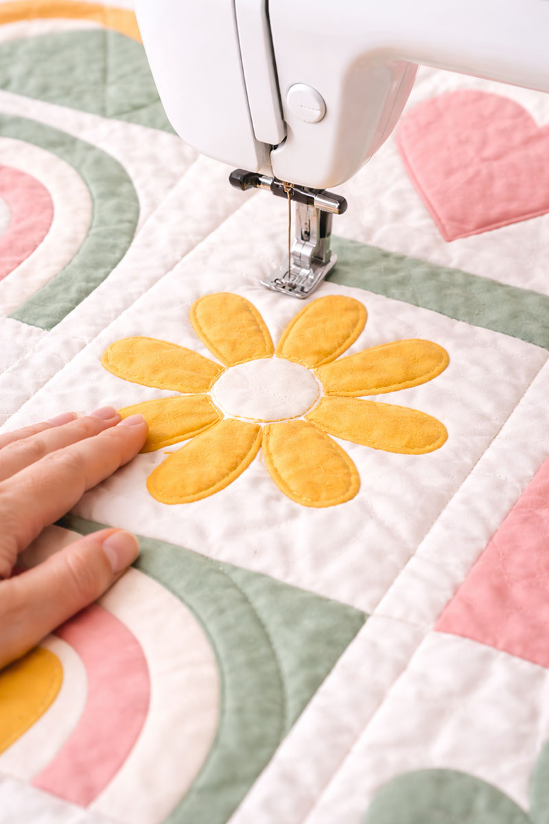 Close-up of stitching around a flower appliqué on a modern rainbow crib quilt pattern