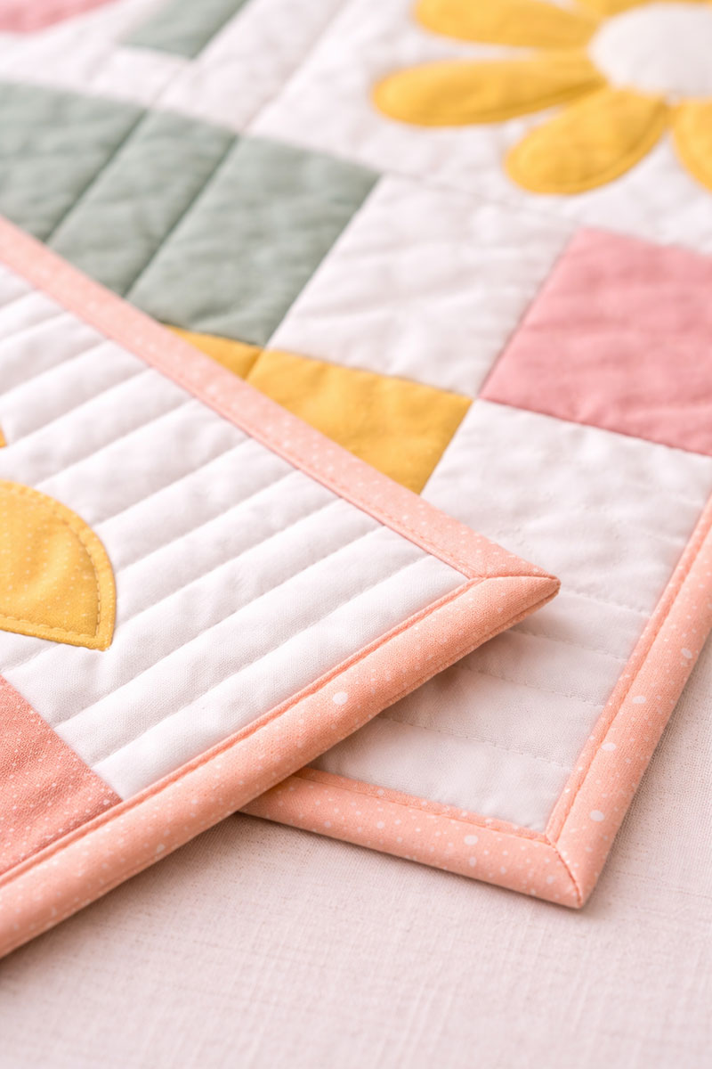 Mitered binding corner detail on a modern baby quilt with pastel rainbow blocks and clean quilting lines