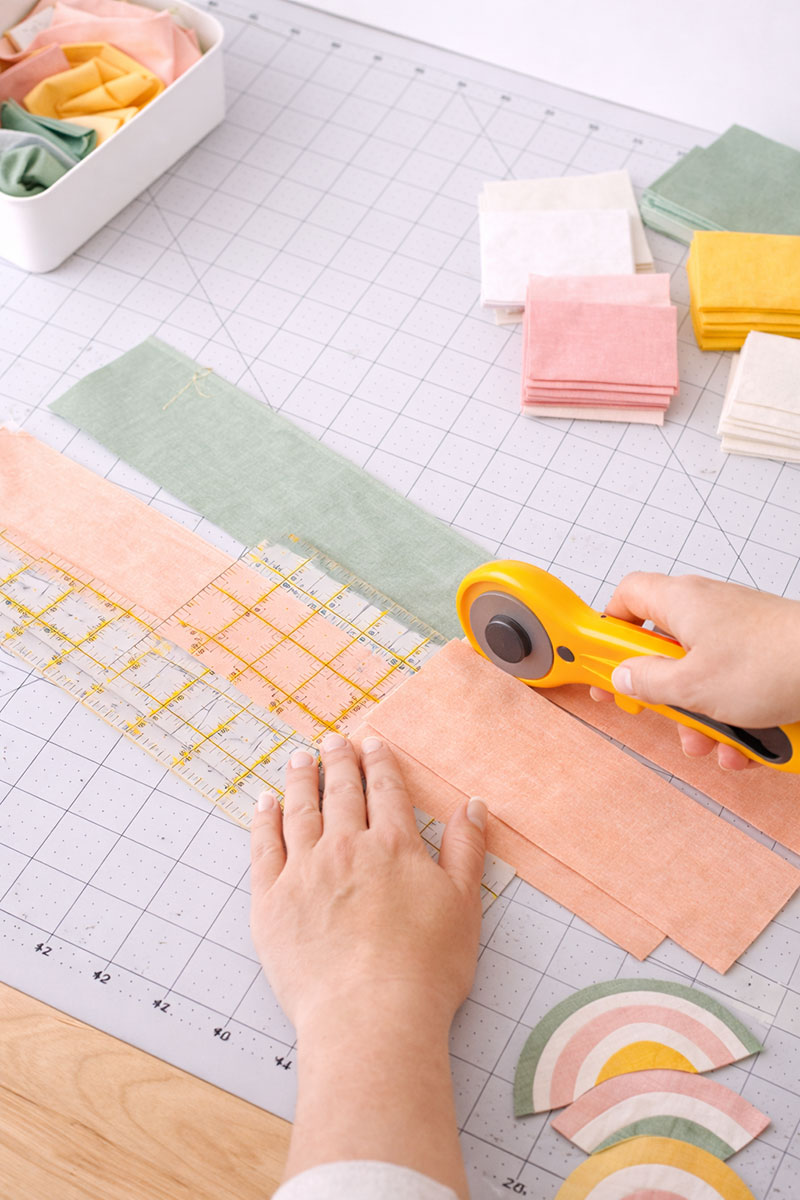 Cutting pastel quilting cotton for a beginner quilt pattern using a rotary cutter and grid cutting mat