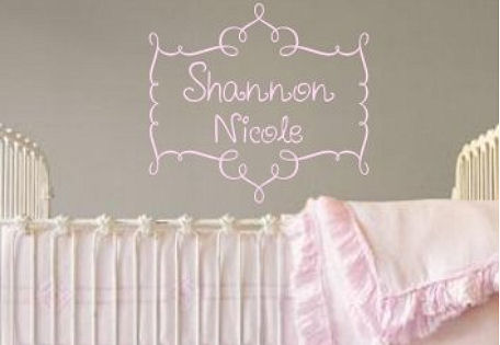 Pink personalized baby girl name decal surrounded with a scroll design on a gray nursery room wall