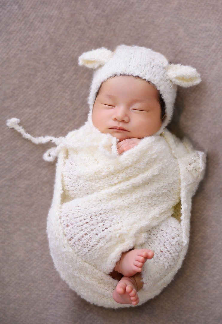 Peaceful, sleeping baby swaddled in organic cotton on an organic mattress