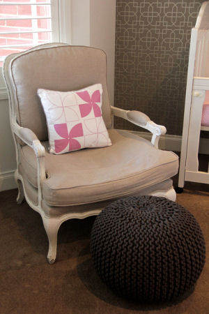 Pink and white square accent pillow in the seating area of a baby girl nursery room