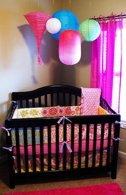 Colorful paper lanterns hung from the ceiling over the crib reflect the bright colors of the custom baby bedding.  