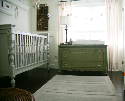 A silver gray baby crib and olive green dresser in a nursery with mint green walls