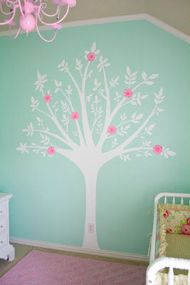 DIY painted tree baby nursery mural on an aqua blue wall in a baby girl room with pink flowers on the branches