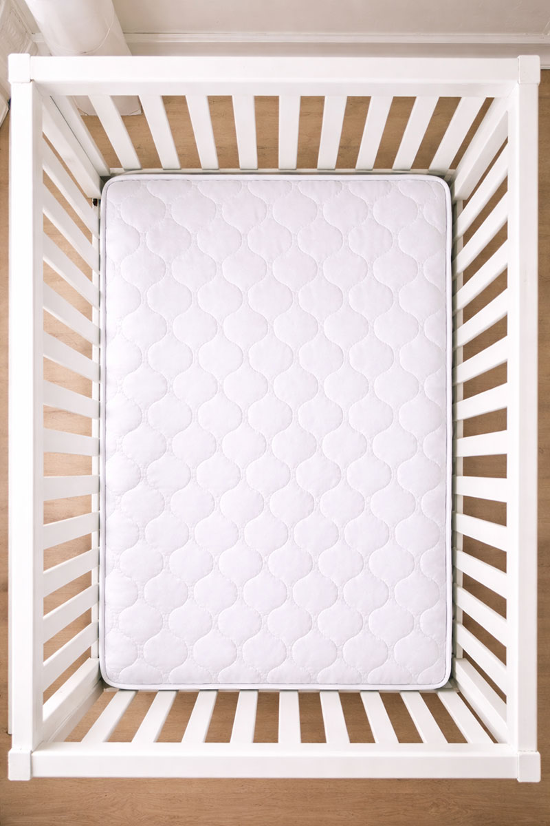 Overhead view into a white crib showing one mattress with rails visible on all sides and a small gap