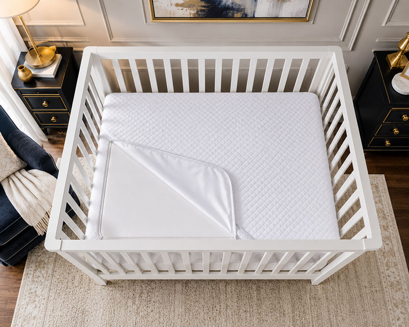 Waterproof crib mattress protector layer on a clean crib mattress in a modern nursery