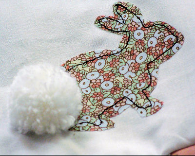 Calico bunny applique with a pom pom bunny tail on patchwork baby crib quilt with fall leaves and tree swing