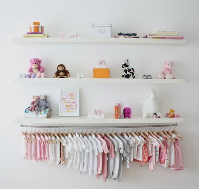 A wall display of wooden shelves with decorations and baby girl outfits organized on matched hangers according to size