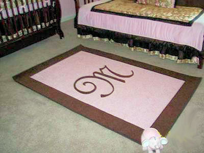 Baby girl's pink and brown custom rectangle nursery area rug with a monogrammed initial in the center and a border.